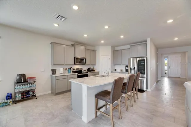 a living room with stainless steel appliances furniture a kitchen view and a refrigerator