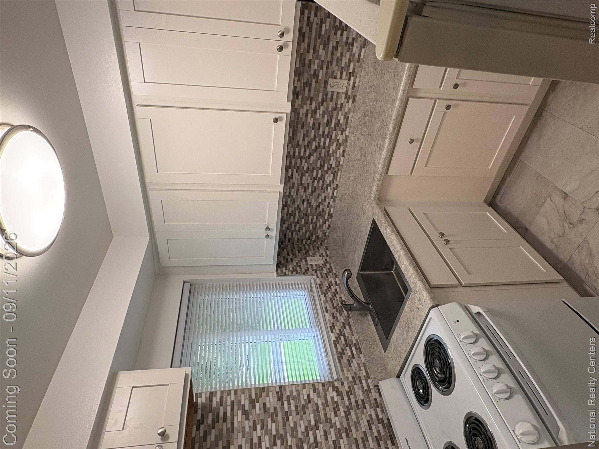 26945 Milford Road, Unit 3 New Hudson, MI 48165 - Photo 9 of 27 White shaker-style cabinetry, mosaic tile backsplash, solid surface countertops, stainless steel sink, and ceramic tile flooring