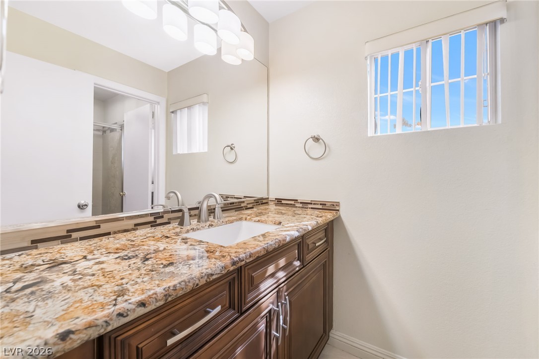 5905 Crumbling Ridge Street Henderson, NV 89011 - Photo 22 of 28 Rich stone counters and warm wood cabinetry define this inviting vanity space.