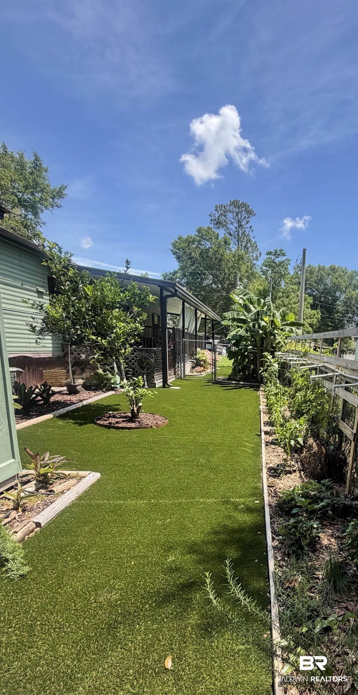 1620 Del Rey Drive Lillian, AL 36549 - Photo 24 of 45 Expansive outdoor space featuring artificial turf, a raised garden bed with plants, and mature trees