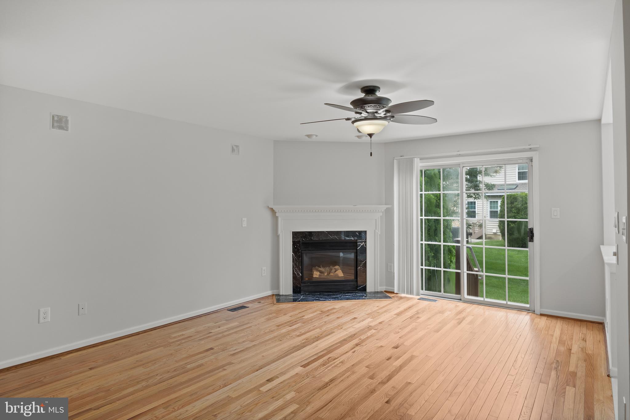 a view of an empty room with wooden floor fireplace and a window