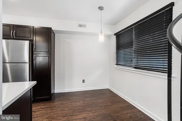 a view of a refrigerator in kitchen and an empty room with wooden floor