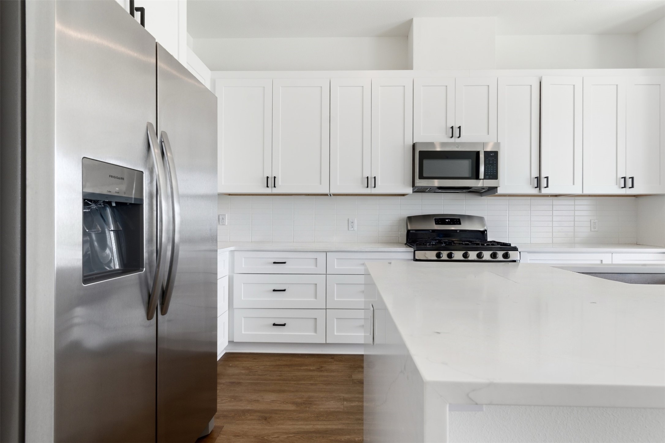 1811 Webberville Road, Unit 1305 Austin, TX 78721 - Photo 2 of 13 Kitchen featuring stainless steel appliances, white cabinetry, tasteful backsplash, dark wood-style floors, and light stone counters