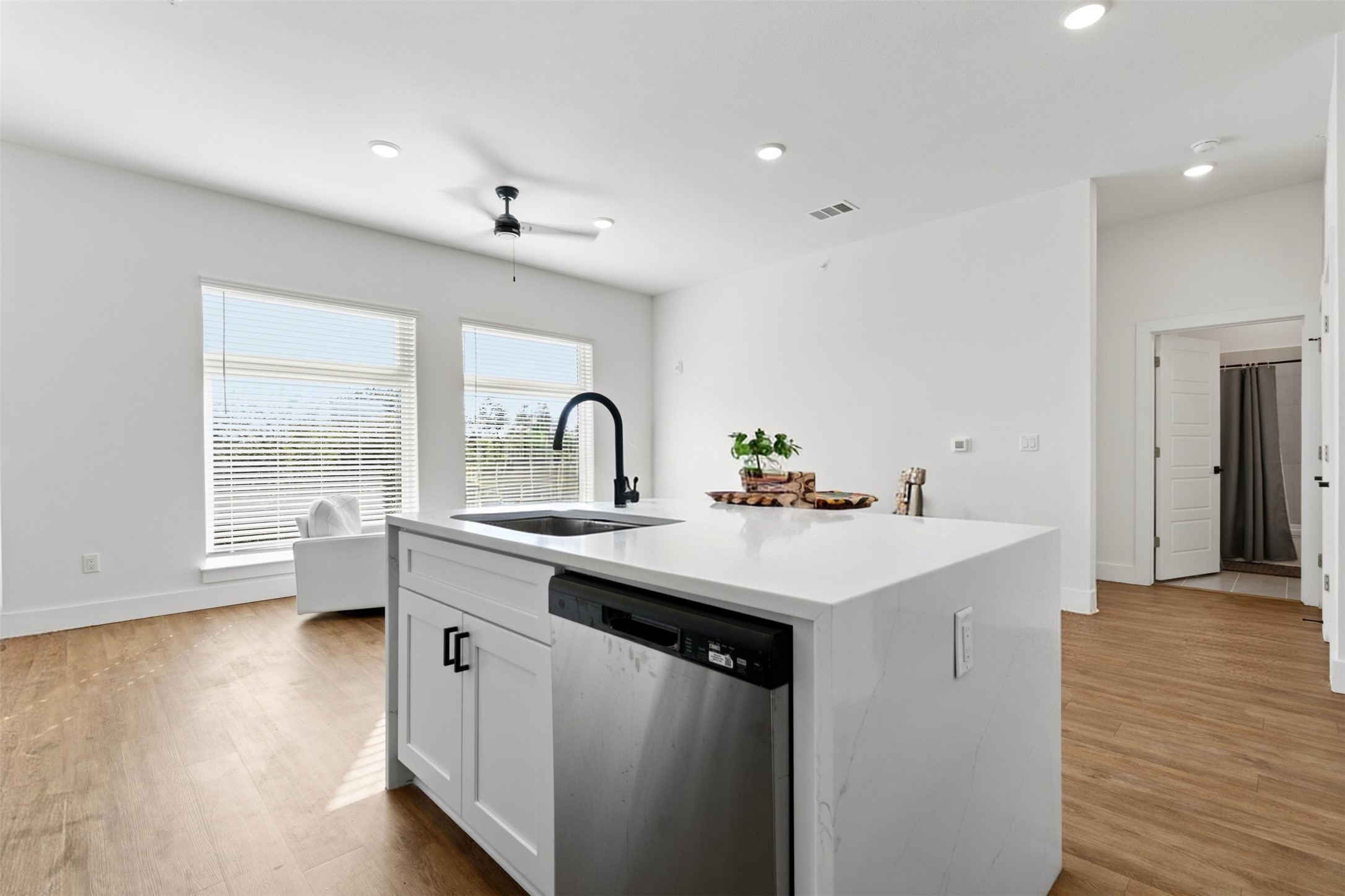 1811 Webberville Road, Unit 1305 Austin, TX 78721 - Photo 3 of 13 Kitchen featuring stainless steel dishwasher, a kitchen island with sink, white cabinetry, light stone countertops, and a ceiling fan