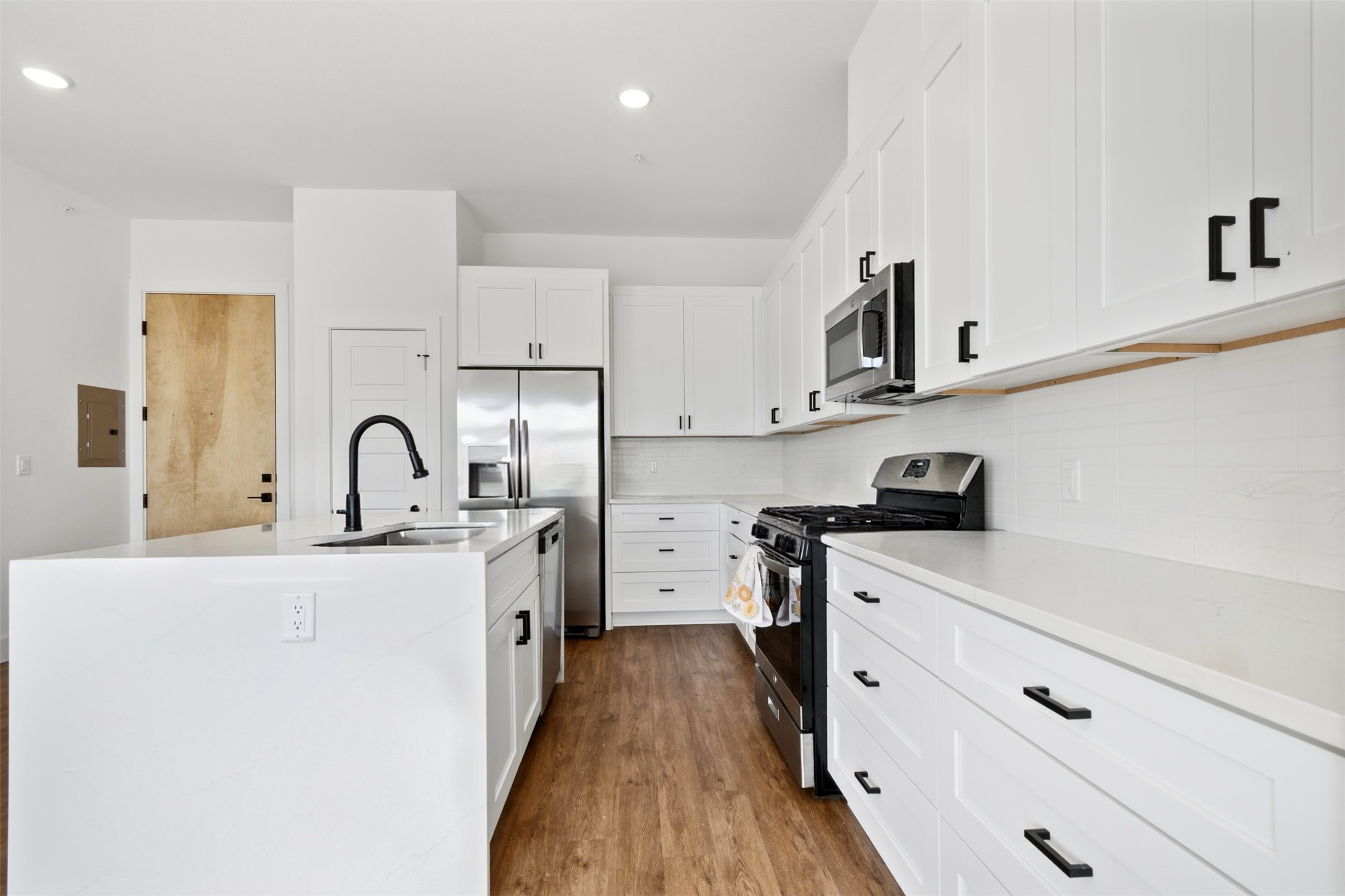 1811 Webberville Road, Unit 1305 Austin, TX 78721 - Photo 4 of 13 Kitchen with stainless steel appliances, light stone countertops, a center island with sink, white cabinetry, and recessed lighting