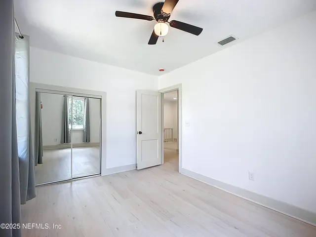a view of an empty room with wooden floor and a ceiling fan