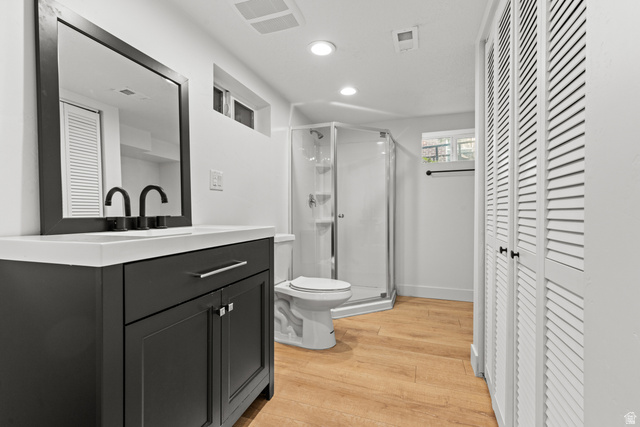 2101 West 3900th Street South Roy, UT 84067 - Photo 25 of 36 Modern bathroom featuring a dark grey vanity with a white countertop and matte black faucets, a corner glass shower enclosure, wood-finish flooring, and white louvered bifold closet doors