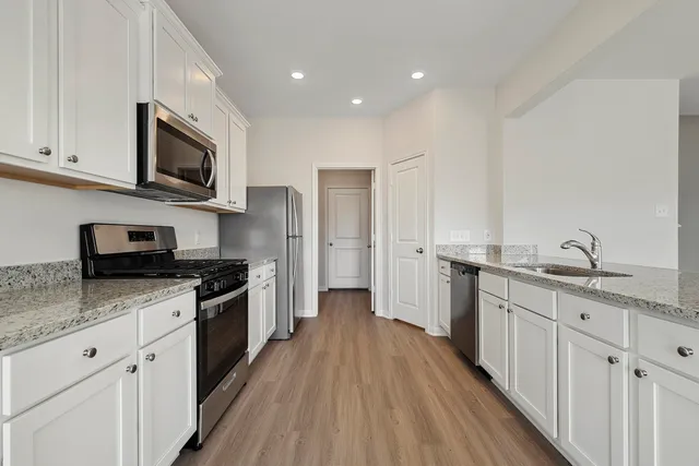 a kitchen with stainless steel appliances granite countertop a stove top oven a sink dishwasher and a refrigerator with wooden floor