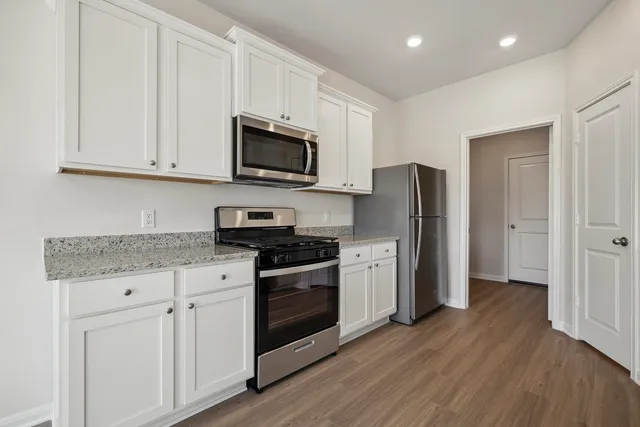 a kitchen with stainless steel appliances granite countertop a refrigerator stove a sink and white cabinets with wooden floor