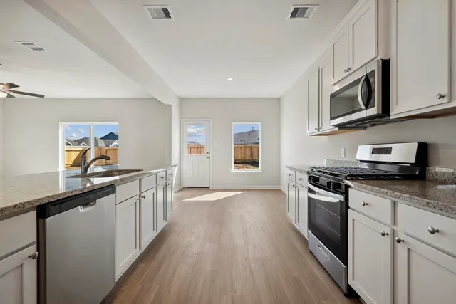 a kitchen with stainless steel appliances a sink dishwasher stove and microwave with wooden floor