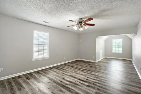 an empty room with wooden floor chandelier fan and windows