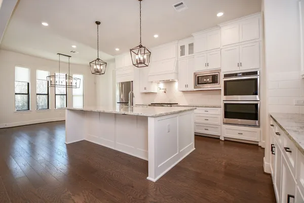 a large white kitchen with stainless steel appliances kitchen island granite countertop a stove a sink a refrigerator and a wooden floor