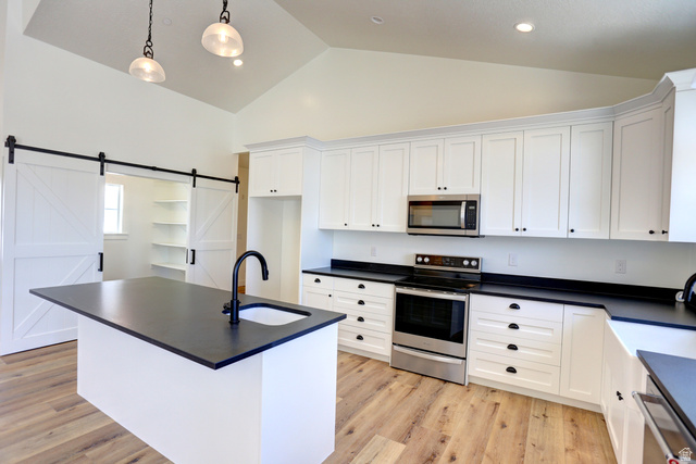 1257 North 1350th Street East Mapleton, UT 84664 - Photo 7 of 34 Vaulted ceiling kitchen featuring white cabinetry, dark countertops, a center island with sink, stainless steel appliances, and wood-finish flooring