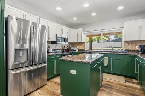 a kitchen with stainless steel appliances granite countertop a refrigerator a sink a stove and a refrigerator