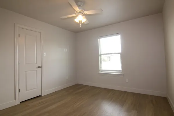 an empty room with wooden floor chandelier fan and windows