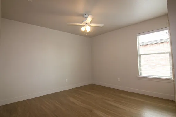 an empty room with wooden floor fan and windows