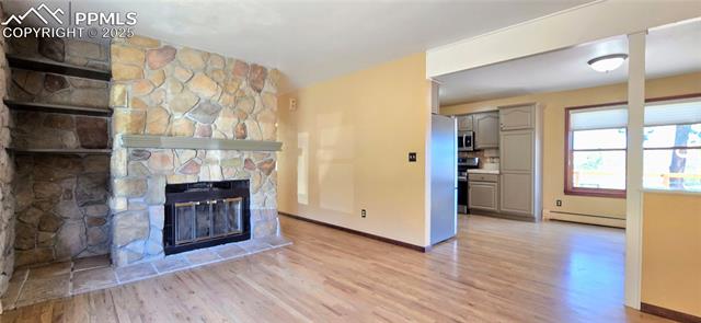 18170 Forest View Road Monument, CO 80132 - Photo 6 of 32 Unfurnished living room with a baseboard heating unit, a stone fireplace, light wood-type flooring, and baseboards
