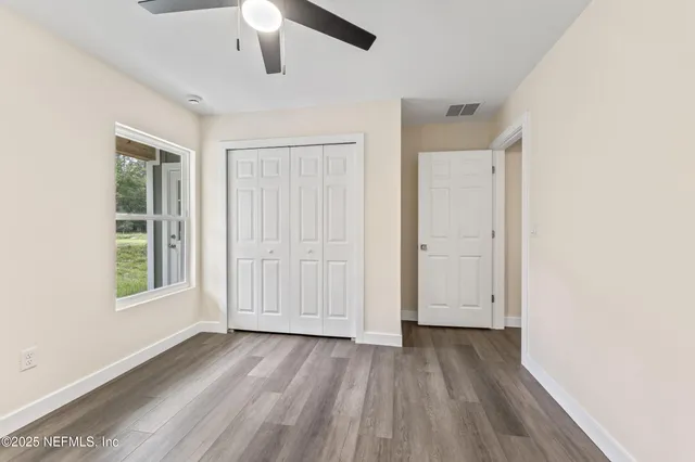 an empty room with wooden floor chandelier fan and windows