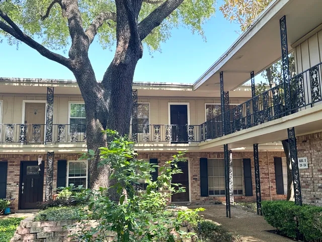 a front view of a house with plants and large trees