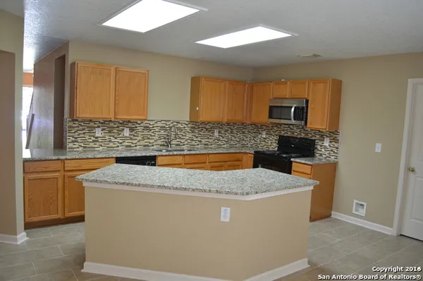 a kitchen with granite countertop a sink a stove top oven and cabinetry