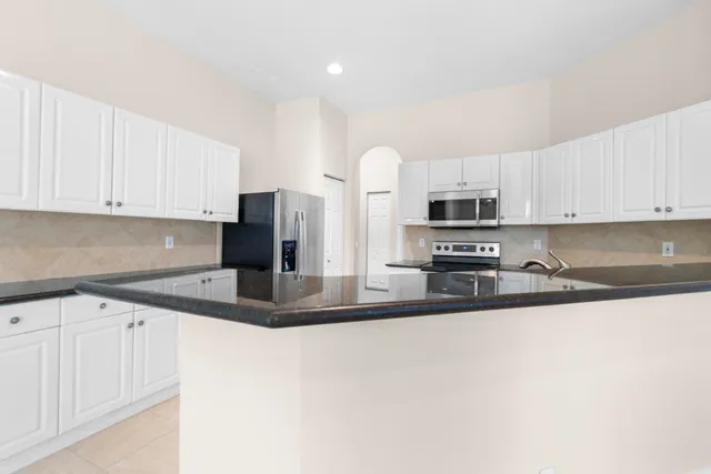 a kitchen with stainless steel appliances granite countertop a sink a stove and a refrigerator with white cabinets