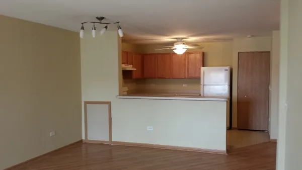 a view of a refrigerator in kitchen and an empty room with wooden floor