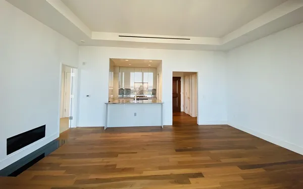 a view of an empty room with wooden floor and a kitchen