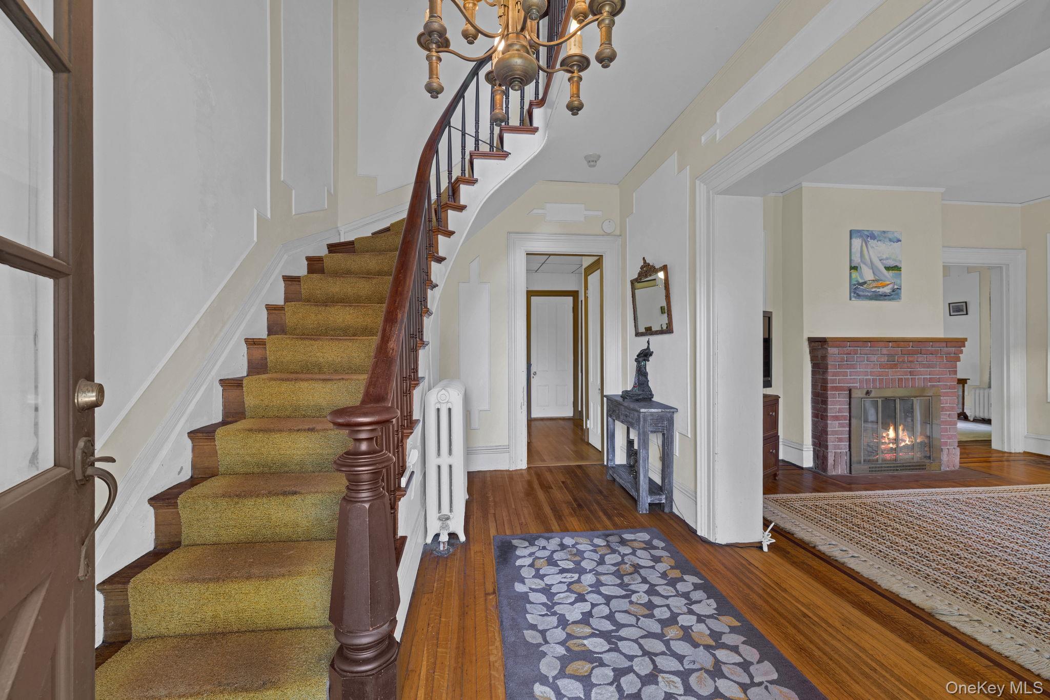 470 Little Britain Road Newburgh, NY 12550 - Photo 16 of 45 Foyer featuring dark wood-style floors, radiator, a brick fireplace, stairs, and a chandelier