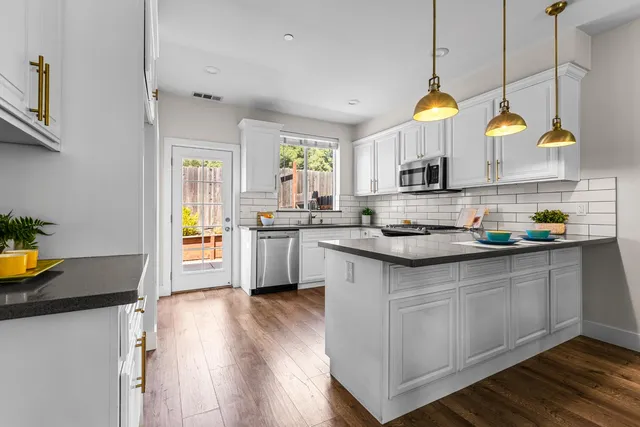 a kitchen with stainless steel appliances a sink a stove a refrigerator a center island and wooden floor