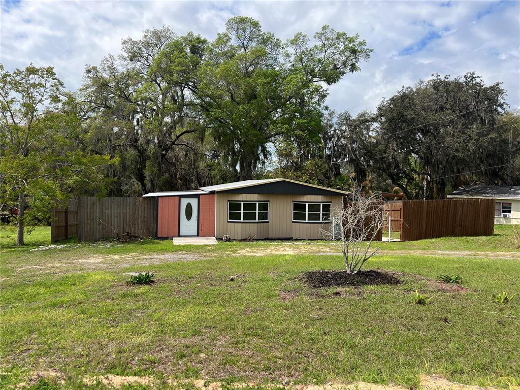 a house that is sitting in the grass with large trees and plants