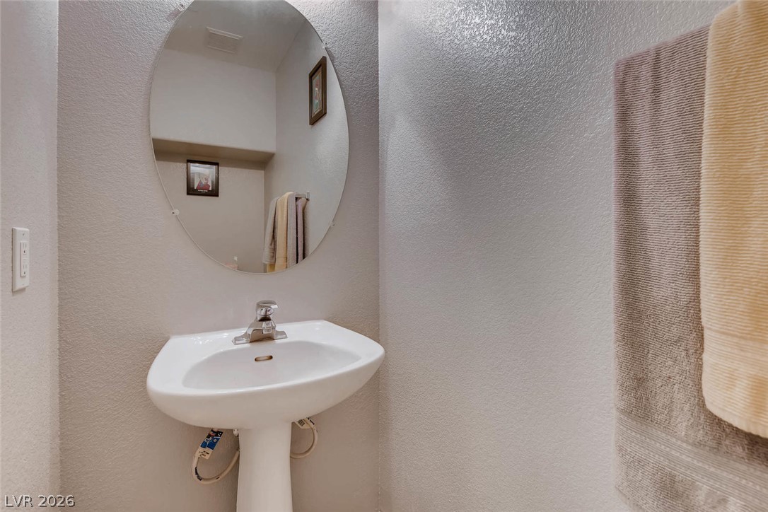 10451 Processor Court Las Vegas, NV 89129 - Photo 14 of 28 A pristine pedestal sink paired with a sleek circular mirror creates a minimalist yet functional bathroom space.