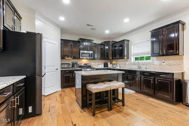 a kitchen with kitchen island granite countertop a stove top oven a sink dishwasher a refrigerator and a dining table with wooden floor