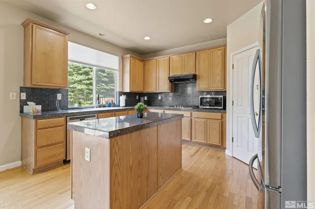 a kitchen with stainless steel appliances granite countertop a refrigerator a sink dishwasher a stove and white countertops with wooden floor