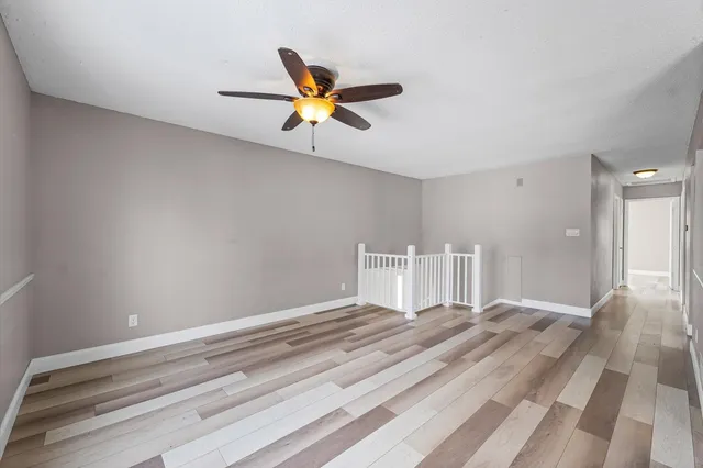 a view of an empty room with wooden floor and a ceiling fan