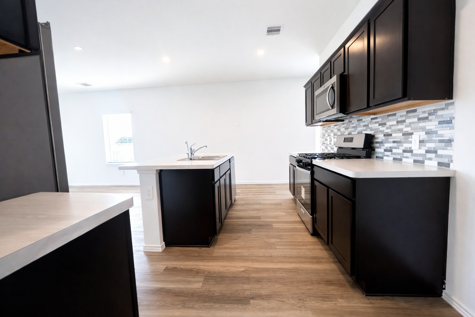 1739 Royal Rim Drive Houston, TX 77014 - Photo 6 of 20 This modern kitchen features sleek dark cabinetry, a stylish tiled backsplash, and stainless steel appliances. The open layout with a central island offers ample counter space and natural light, perfect for cooking and entertaining.