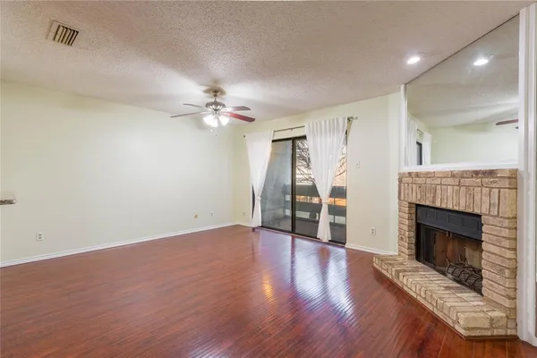a view of an empty room with wooden floor fireplace and a window