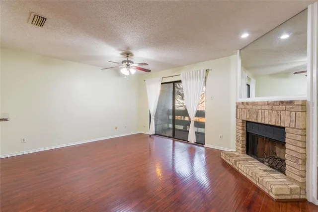a view of an empty room with wooden floor fireplace and a window
