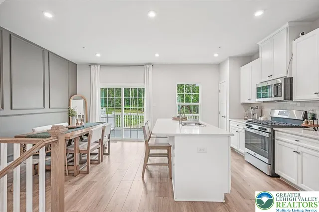a open kitchen with stainless steel appliances granite countertop a stove top oven a sink dishwasher a dining table and chairs with wooden floor