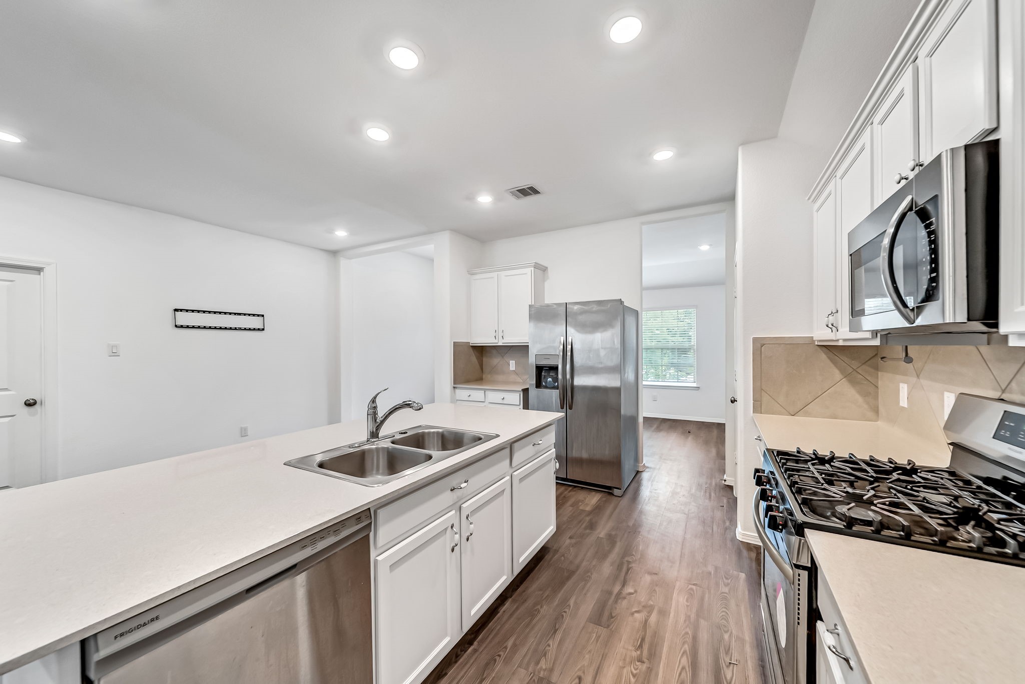 2847 Mistygate Court Conroe, TX 77301 - Photo 6 of 27 This modern kitchen features stainless steel appliances, a spacious island with dual sinks, white cabinetry, and wood flooring, offering a bright and functional space for cooking and entertaining.