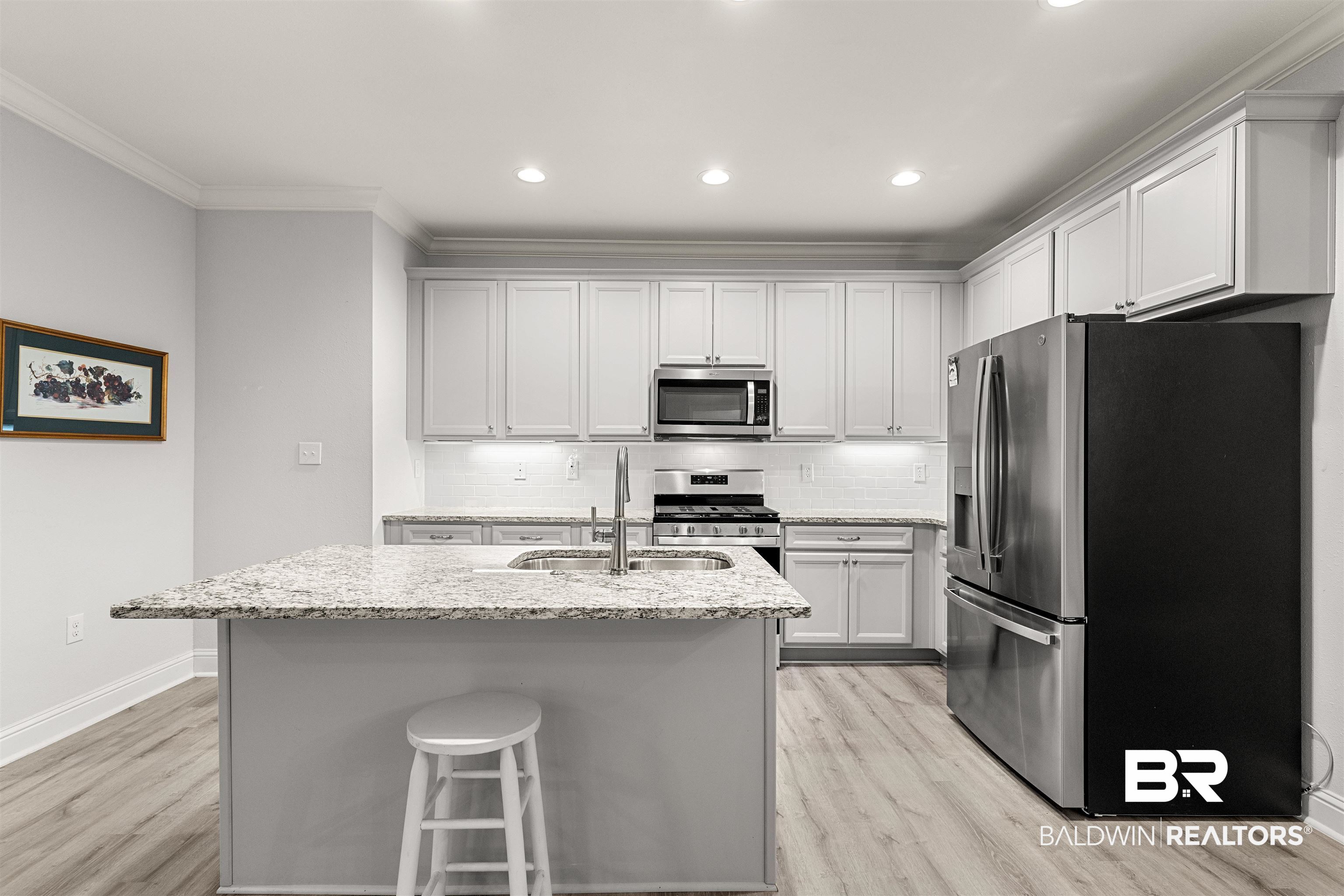 702 Holmes Avenue, Unit 702 Foley, AL 36535 - Photo 8 of 33 Kitchen featuring a center island with sink, stainless steel appliances, light stone counters, white cabinets, and backsplash