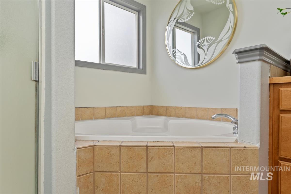 80 Cobblestone Court Middleton, ID 83644 - Photo 23 of 48 Corner soaking tub with tiled surround, chrome fixtures, and frosted window