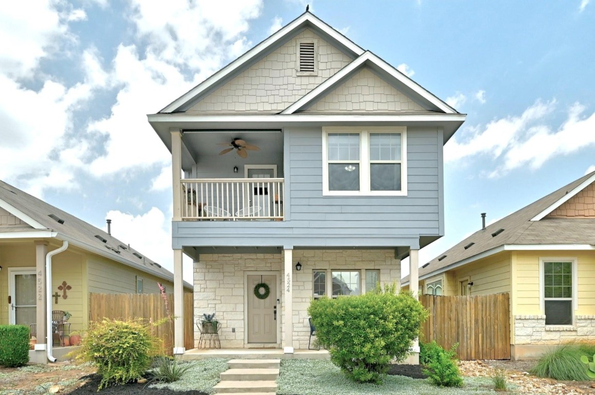 View of front of home featuring stone siding, a balcony, a ceiling fan, and a porch