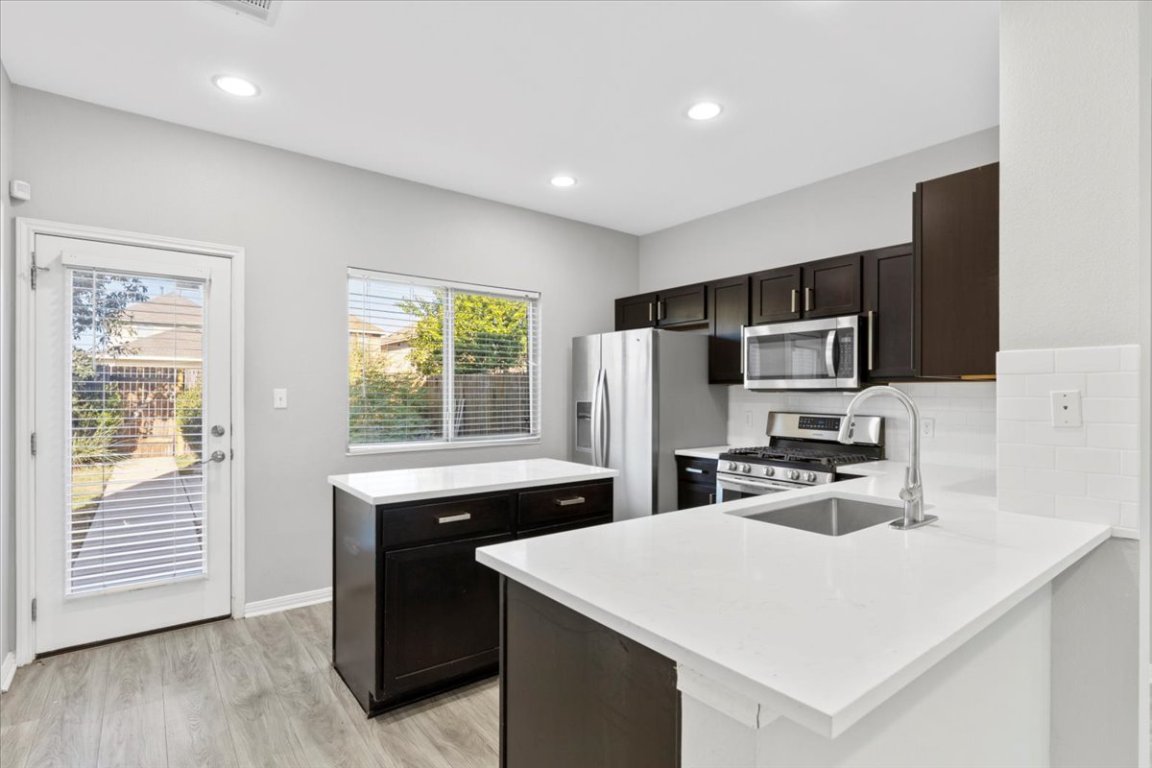 4524 Kind Way, Unit 257 Austin, TX 78725 - Photo 2 of 16 Kitchen with a kitchen island, stainless steel appliances, light stone countertops, light wood-style flooring, and tasteful backsplash