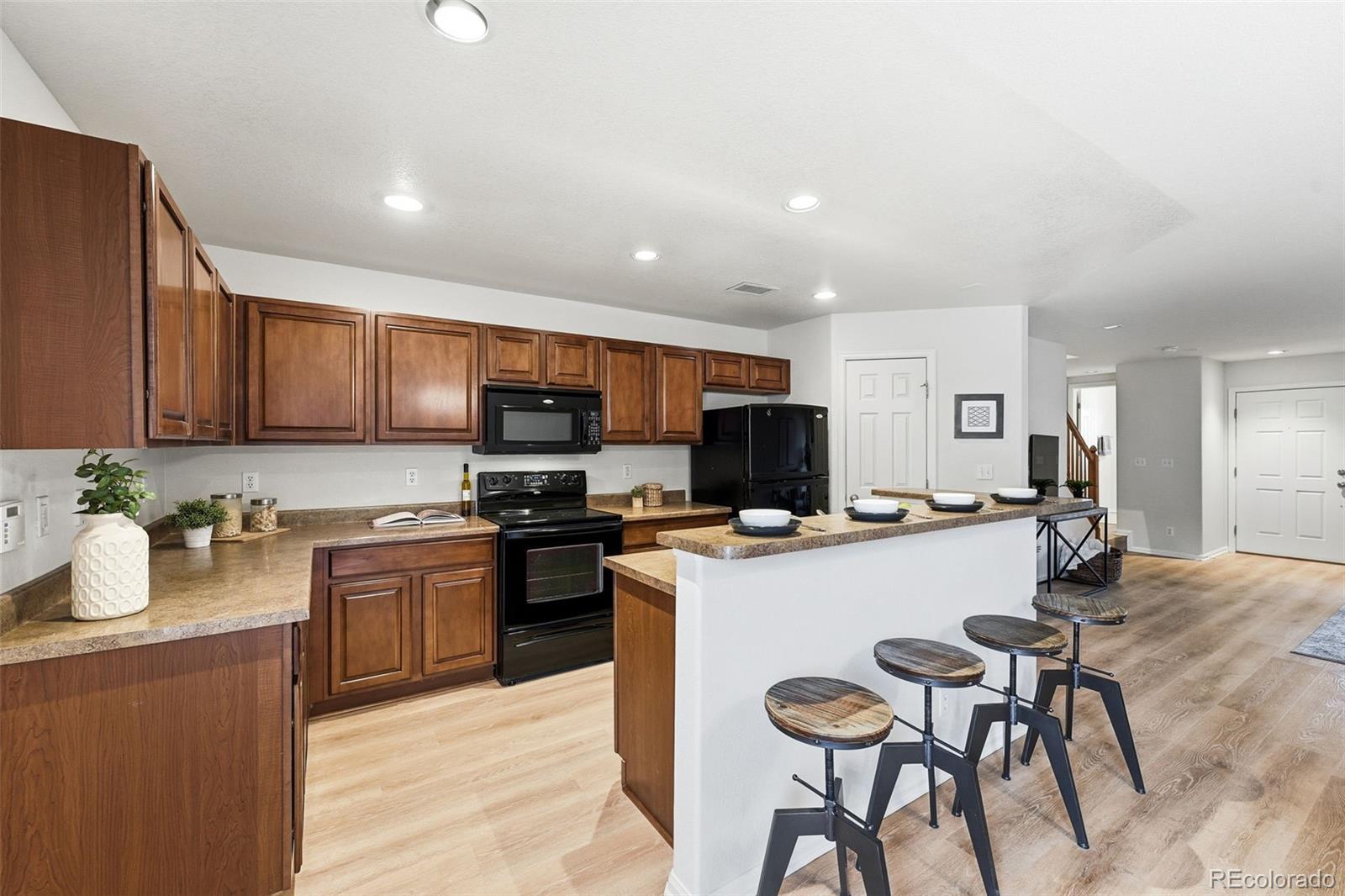5811 Ceylon Street Denver, CO 80249 - Photo 16 of 43 a kitchen with stainless steel appliances a stove top oven a sink a refrigerator a dining table and chairs with wooden floor