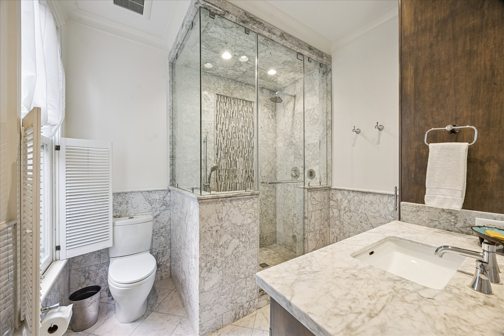 2368 Timber Lane Houston, TX 77027 - Photo 33 of 46 The luxurious en suite bath is thoughtfully finished with Carrara marble flooring, custom cabinetry with specialized pull-out laundry storage, elegant marble countertops, a Toto undermount sink, and polished Hansgrohe Axor fixtures. The oversized walk-in steam shower creates a spa-like experience with a rain shower head, separate handheld sprayer, and a floating bench designed for comfort and relaxation.