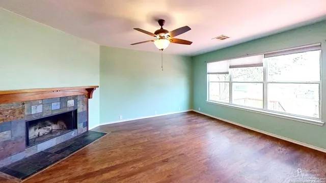 an empty room with wooden floor a ceiling fan and a fireplace
