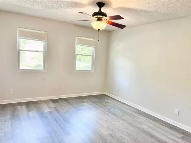 an empty room with wooden floor chandelier fan and windows