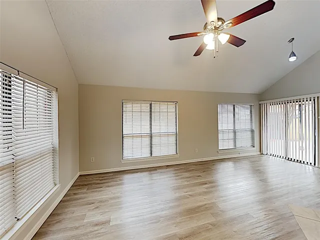 an empty room with wooden floor fan and windows