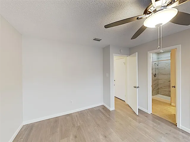 a view of an empty room with wooden floor and a ceiling fan