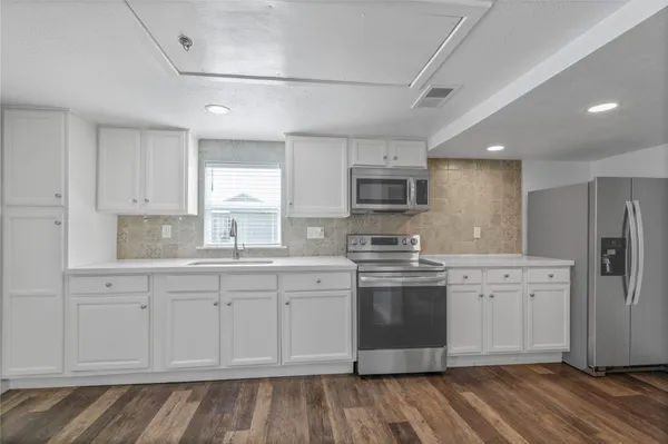 a kitchen with stainless steel appliances granite countertop a stove a sink dishwasher and a refrigerator with wooden floor